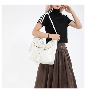 Close-up of white leather handbag featuring a large bow and silver stud details