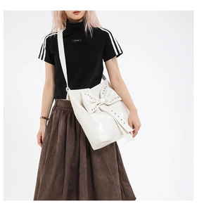 Detail of white PU leather bag with large bow and silver metal rivets on shoulder strap