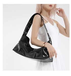 Détail du sac croissant en cuir verni noir avec large bandoulière et œillets argentés