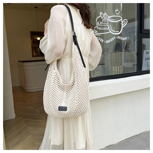 Detail of white handmade crochet hobo bag with delicate mesh texture and black shoulder strap