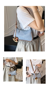 Detail of light blue textured shoulder bag with brown leather strap and wooden horse charm