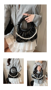 Detail of black pleated cloud bag featuring pearl chain and gold leather crossbody strap
