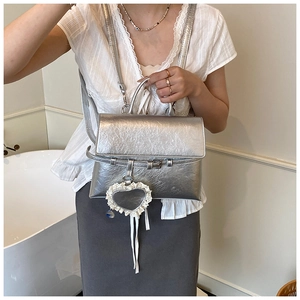 Detailed view of silver PU leather backpack with a lace heart charm on a female model