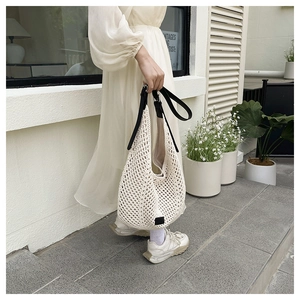 Chic beige woven shoulder tote bag with black handles styled on a model in sunlight