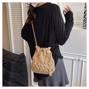 Detailed close-up of beige woven straw bucket bag with floral patterns and tassel drawstring
