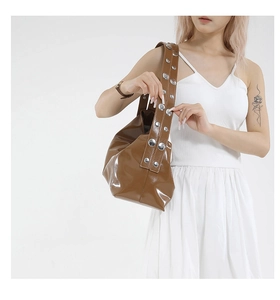Brown glossy shoulder bag featuring large silver metal rivets on the strap worn by model