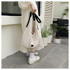 Detail of hand-woven beige crochet tote bag featuring high-contrast black shoulder straps