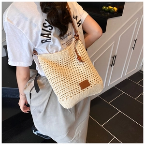Detail of woven straw tote bag with brown leather strap and wood bead drawstring