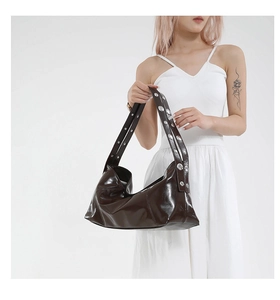 Close-up of brown patent leather crescent bag with silver studded shoulder strap detail