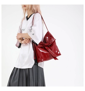 Detail of red glossy shoulder bag featuring large bow and metallic rivet accents