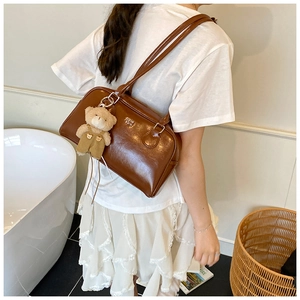 Gros plan d'un sac à bandoulière en cuir marron poli avec une peluche ours et un logo