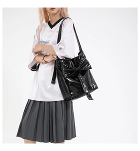 Detail of black patent leather tote bag with a large bow and silver rivet studs