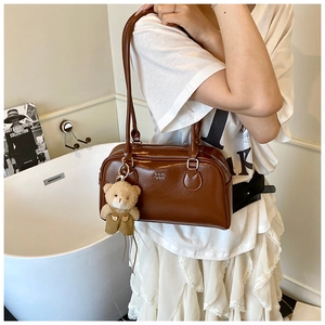 Détail d'un sac bandoulière en cuir marron brillant avec charm ours en peluche