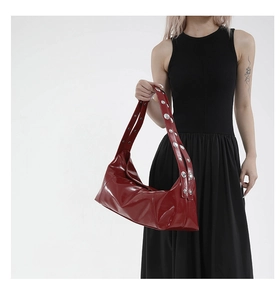 Detail of red patent leather shoulder bag featuring wide strap with silver metal rivets