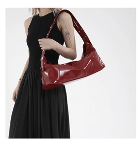 Detail of dark red patent leather shoulder bag with silver eyelets on wide strap