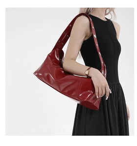 Detail of red patent leather crescent bag with silver rivet studs on wide shoulder strap