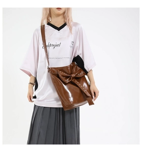 Detail of a brown glossy leather crossbody bag featuring a large studded bow decoration