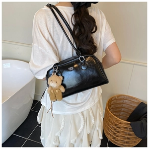Détail du sac Boston en cuir verni noir avec un charmant pendentif ours en peluche doux