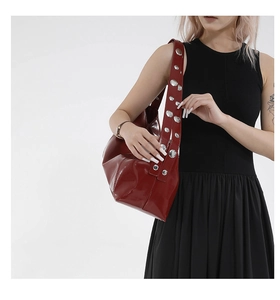 Detail of burgundy patent leather bag featuring silver metal rivets on wide shoulder strap