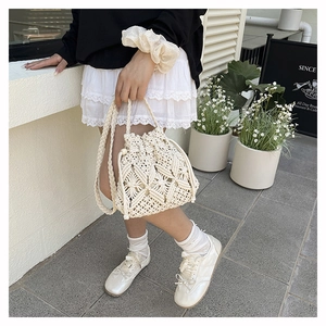 Close-up of a cream crochet bucket bag with wheat pattern texture and a long woven strap