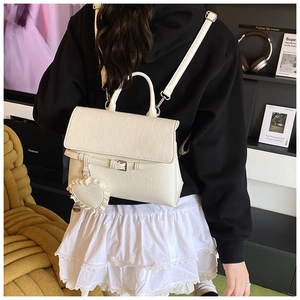 Detail view of a cream PU leather backpack with a heart lace charm on a model