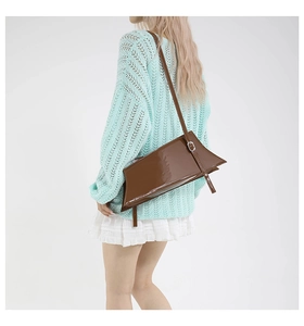 Détail d'un sac à bandoulière marron en cuir verni brillant avec un design asymétrique et boucle argent