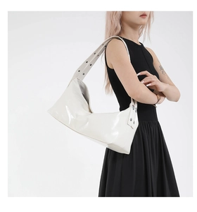 Close-up of white patent leather crescent bag featuring silver studs on the wide shoulder strap