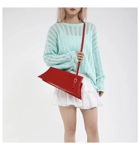Détail d'un sac à main rouge en similicuir brillant porté avec une tenue d'été