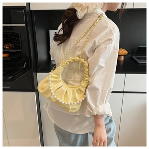 Detail of a yellow dumpling cloud bag with pearl strap and pleated handle on a model