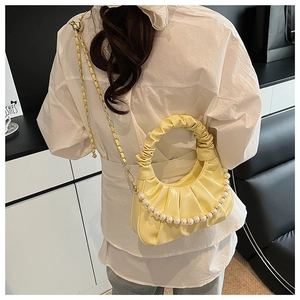 Detail of yellow ruched dumpling bag with pearl strap and gold chain worn crossbody