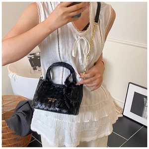 Détail du sac seau en cuir noir tressé avec bandoulière chaîne dorée et logo gravé