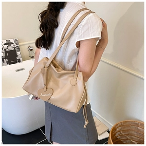 Detail of beige leather shoulder bag featuring a heart-shaped tag and drawstring closure