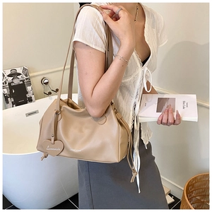 Detail of beige pleated hobo bag with heart charm and brand logo embossed on the surface