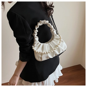 Close-up of ruched white shoulder bag with decorative pearl beads on a model wearing black