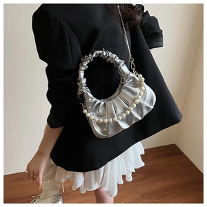 Detail of silver pleated dumpling bag with pearl handle and metal chain on a model