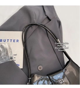 Détail d'un sac bandoulière en cuir verni noir avec logo métallique sur costume gris