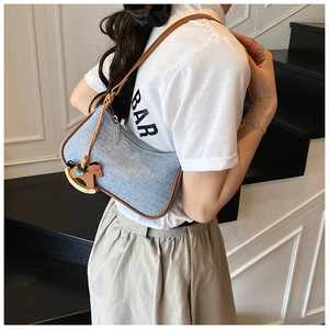 Detail of light blue fabric underarm bag with brown leather trim and horse charm