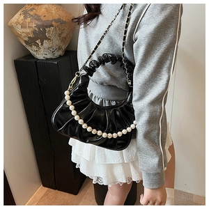 Detail of black pleated cloud bag featuring oversized pearl strap and gold chain accent