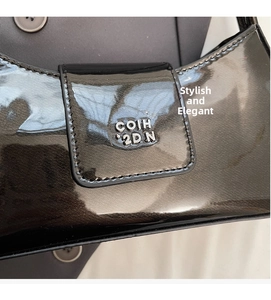 Détail du sac en cuir verni noir brillant avec logo métallique argenté et texture chic