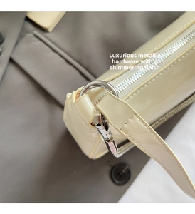Gros plan sur les ferrures argentées et le cuir verni brillant du sac baguette blanc crème