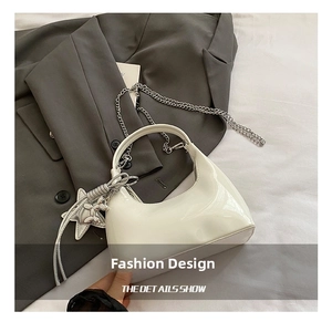 Detail view of white patent leather bucket bag with silver chain strap and star charm