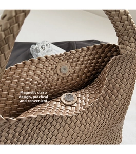 Detail view of woven champagne gold handbag showing magnetic snap button closure