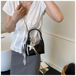 Model wearing a black patent leather bucket bag with silver chain and star charm
