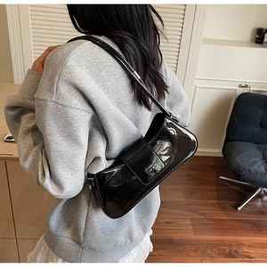 Détail du sac baguette en cuir verni noir avec logo argenté porté à l'épaule