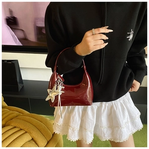 Detail of burgundy patent leather underarm bag featuring a metallic star charm
