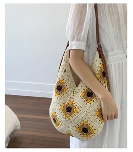 Close-up of knit tote bag with sunflower patterns and brown leather strap on a model