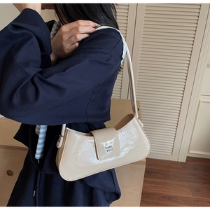Gros plan du sac baguette en cuir verni beige avec logo en métal sur l'épaule