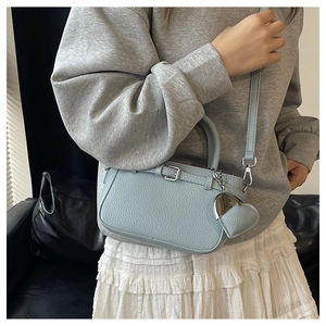 Detail of light blue lychee pattern leather handbag with heart-shaped charm and strap