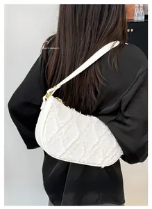 Close-up of white denim half-moon underarm bag with frayed edges and golden buckle