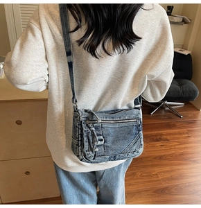 Detail of blue washed denim crossbody bag showing multiple zippers and vintage texture